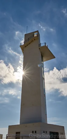 Faro de Irta, una torre de hormigón blanco a contraluz bajo un cielo azul con nubes en el Parque Natural de la Sierra de Irta
