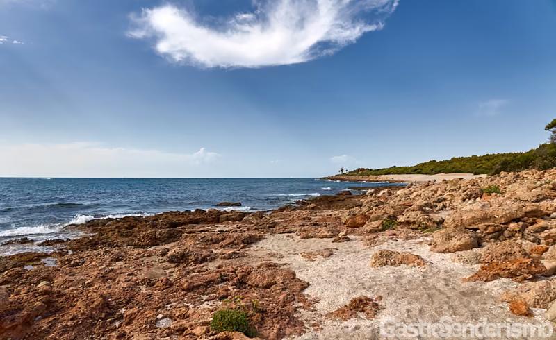Playa de roca y arena en la Sierra de Irta, Alcossebre, mostrando el mar a la izquierda y el faro de Irta al fondo a la derecha