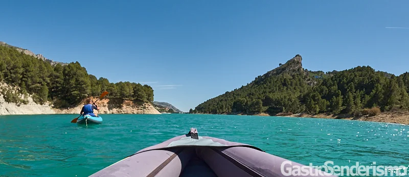 Persona remando en un kayak azul por las aguas turquesas del embalse de Guadalest frente a una pared rocosa.