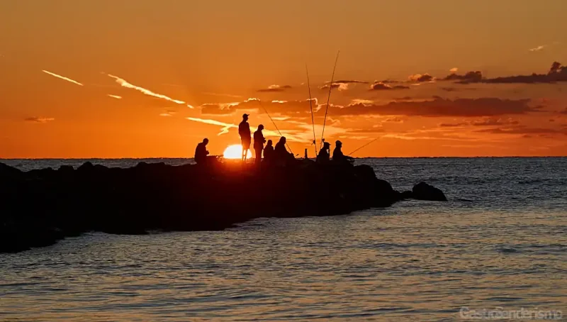 Siluetas de pescadores al amanecer en un espigón de la playa de Port Saplaya, Alboraya, Valencia, con el sol naranja sobre el mar